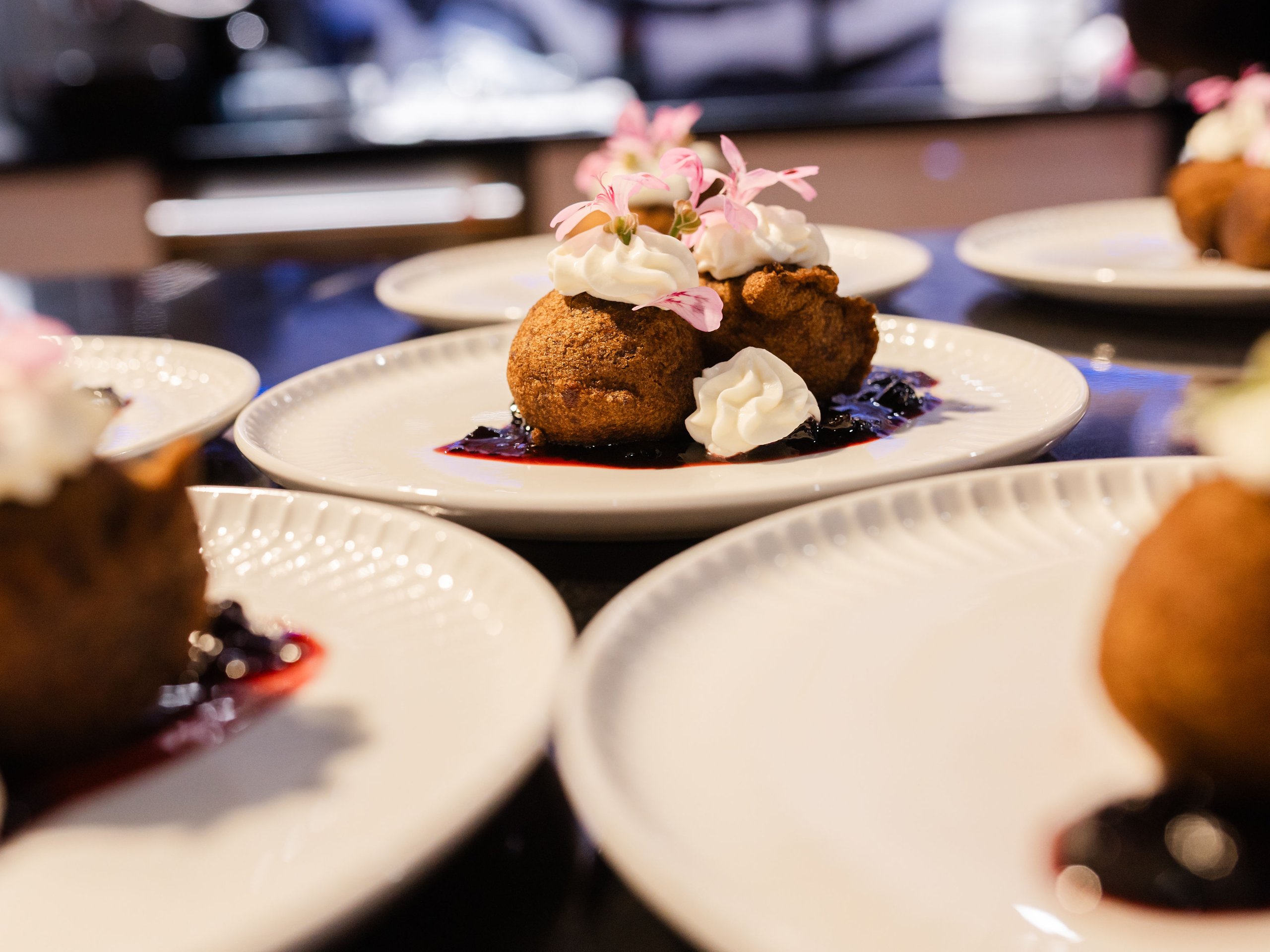 Brown pastries with whipped cream, pink flowers, and berry sauce on a white plate.